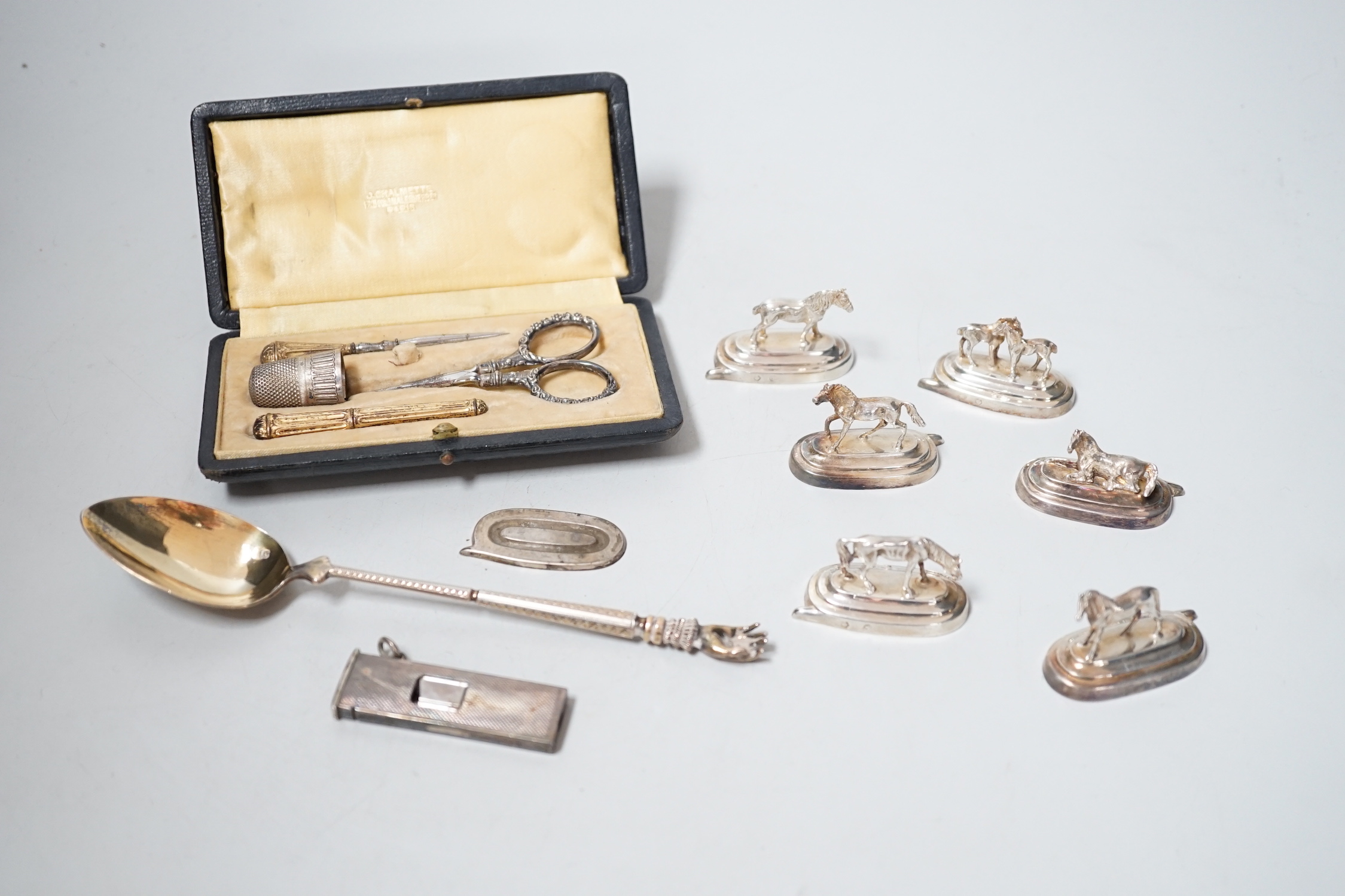 Six assorted Spanish white metal horse menu holders, 43mm, a cased necessaire set, a cigar cutter and a French white metal spoon with hand terminal.